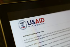 A computer screen displays the USAID logo, which stands for the United States Agency for International Development, along with the slogan "From the American People." Below the logo, there is text about a "Notification of Administrative Leave," though the body text is partially blurred and not fully readable.
